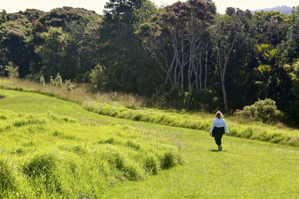 Image of a woman walking through an open green field bordered by woodland