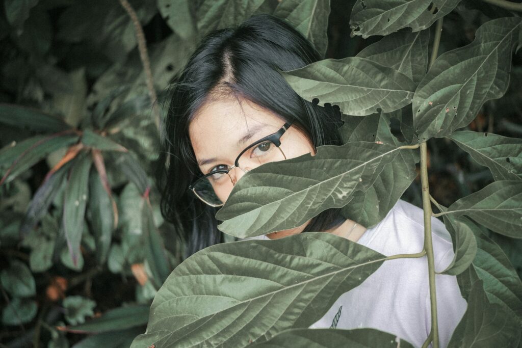 A girl with her face obscured behind a leaf
