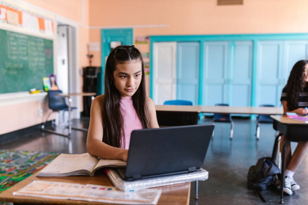A girl sitting at a desk in school and working on a laptop computer