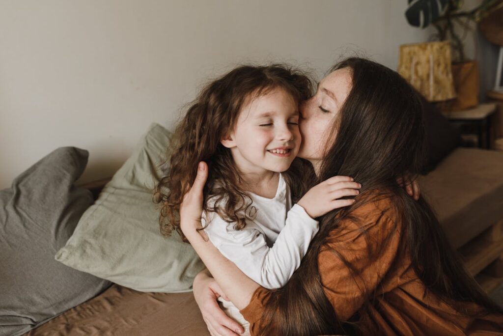 A woman hugging and kissing her young daughter on the cheek